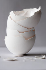 Stack of white eggshells with broken pieces in foreground on gray background, vertical