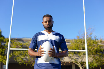 Naklejka premium Rugby player holding ball on field, preparing for game under clear sky