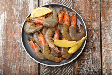 Fresh raw shrimps and lemon on wooden table, top view