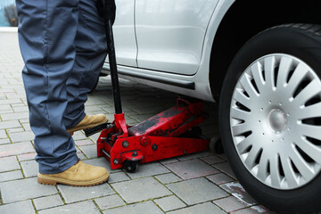 Auto mechanic lifting car with scissor jack outdoors, closeup