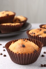 Delicious muffin with chocolate chips on light grey table, closeup