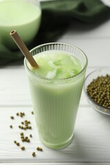 Fresh mung bean juice with ice in glass and seeds on white wooden table, closeup