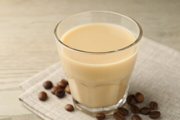Coffee cream liqueur in glass and beans on table, closeup