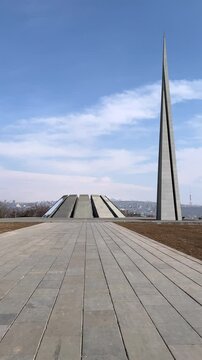 Vertical 4K street video. Man in black walks with his back to memorial complex in Yerevan dedicated to victims of Armenian genocide of 1915 on hill of Tsitsernakaberd. Armenia. Blue sky. Pavement tile