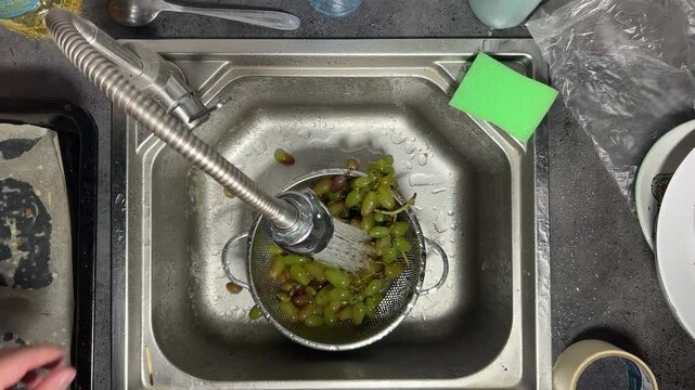 4K video. Top view. Man washes green grape in colander in metal sink in kitchen under faucet with shower. Process of preparing healthy food for breakfast, lunch, salad, eat, dinner. Male hand close up