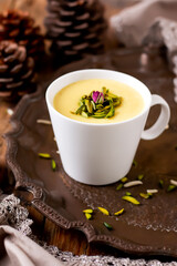 Saffron Custard garnished with pistachios and rose petals served in a white cup on a decorative tray side view aromatic Indian dessert