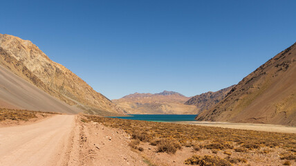 Panoramic view of a road leading to the El Yeso Reservoir between the mountains, under a blue sky in Chile.