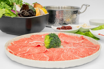 A mouthwatering selection of beef hot pot ingredients is beautifully arranged, featuring tender, thinly sliced beef ready to be cooked in a steaming, flavorful broth. The marbled beef glistens