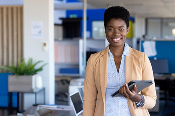 In office, businesswoman holding tablet and smiling confidently in modern setting, copy space