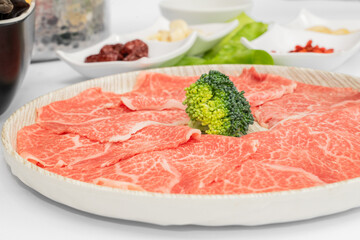 A mouthwatering selection of beef hot pot ingredients is beautifully arranged, featuring tender, thinly sliced beef ready to be cooked in a steaming, flavorful broth. The marbled beef glistens