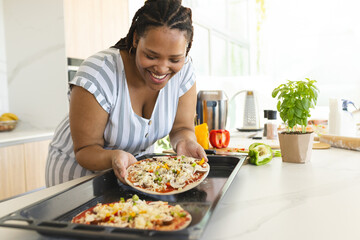 Smiling woman preparing homemade pizza in modern kitchen with fresh ingredients