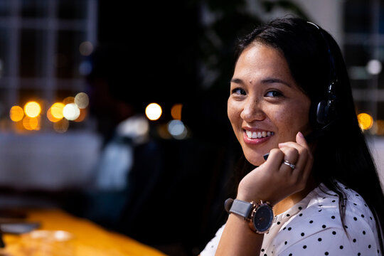 Smiling woman wearing headset working late at office, providing customer support, copy space