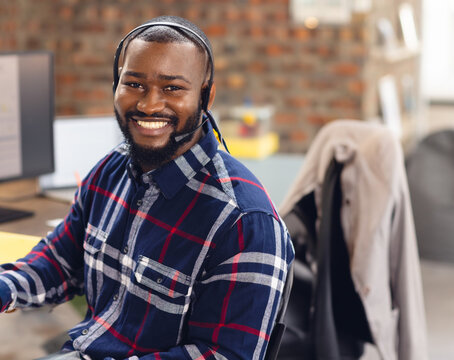 Smiling man in plaid shirt using headset while working at office desk