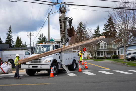 Temporary wood powerline pole cut off and being lifted out of place by utility digger derrick truck with pole setting equipment, lineman helping guide, infrastructure upgrade supporting new housing de