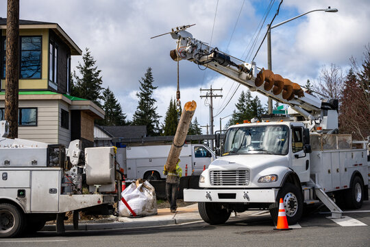 Temporary wood powerline pole cut off and being lifted out of place by utility digger derrick truck with pole setting equipment, lineman helping guide, infrastructure upgrade supporting new housing de