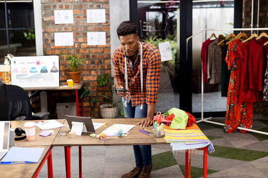 In studio, fashion designer planning new collection using smartphone and tablet