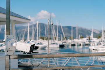 Fototapeta premium White CCTV camera on a pole on the shore of the marina