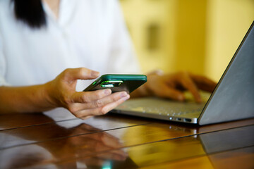 Businessperson Using Smartphone While Working on Laptop at Desk