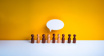 Diverse wooden figures stand in a row beneath a blank speech bubble against a bright yellow backdrop.  Symbolizing communication, diverse voices and collective expression.