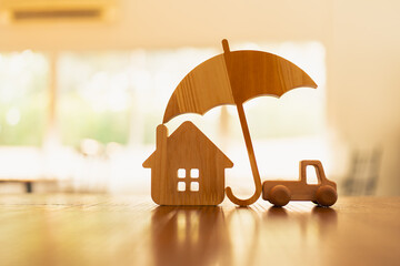 A house and car model with an umbrella in the center and a businessman's hands are counting dollar...