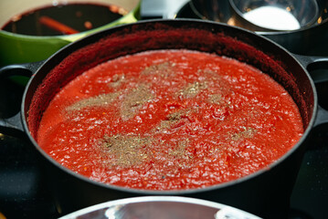 Homemade tomato sauce simmering in cast iron pot. A rich and flavorful homemade tomato sauce cooking in a black cast iron pot, seasoned with herbs and spices, perfect for pasta or pizza.