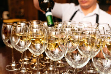 Bartender pouring white wine into multiple glasses.