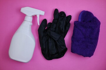 Cleaning accessories spray bottle, rag and black gloves isolated on pink background. Concept for...