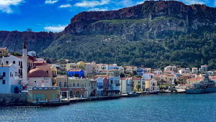 Colorful Waterfront Buildings And Mosque In Kastellorizo Island, Greece, With Mountain Backdrop And Clear Blue Sea, Idyllic Summer Destination, Traditional Architecture, Perfect For Travel And Tourism