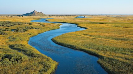 Obraz premium Serene river winding through lush fields with a distant hill under a clear blue sky.