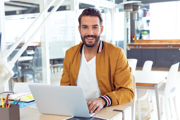 Smiling man using laptop at office desk, working confidently on project