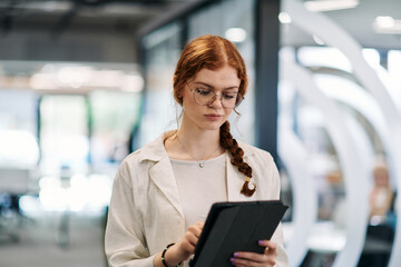 A business woman with orange hair self confident, fully engaged in working on a tablet, exuding...