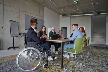 A diverse group of business professionals, including a man in a wheelchair, collaborate during a...