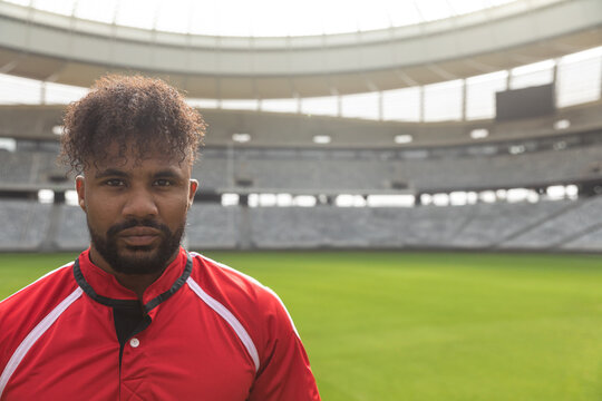 Rugby player in red jersey standing confidently in empty stadium, copy space
