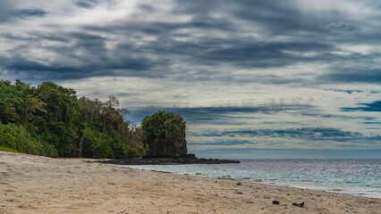 A secluded sandy beach on the coast of a tropical island. The turquoise ocean is calm. A green hill, a picturesque cliff in the distance. Blue sky, clouds. Madagascar. Nosy Tanikeli 