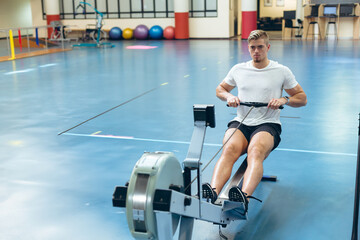Man exercising on rowing machine in gym, focused on fitness routine, copy space