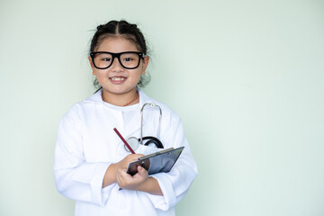 asian girl kid in laboratory gown, writing in a notepad and with a stethoscope, acting like medical practitioners such as doctor, nurse or caregiver to show the benefit of science