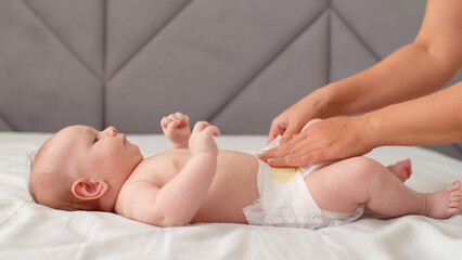 Mother changing the diaper of her newborn baby. Mother changes a diaper on her infant baby at home. Mom puts diapers on her newborn infant, on a changing table.