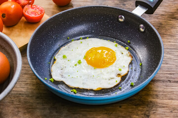fried egg in a pan with tomatoes and ingredients on a wooden table