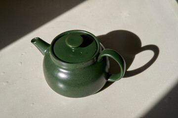 green pottery teapot with its shadow in sunlight