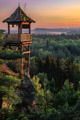 Fototapeta premium Rustic Watchtower Overlooking Lush Forest with Distant Misty Mountains at Dawn or Dusk