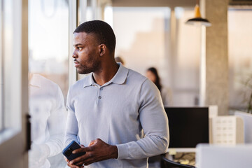 Pensive businessman holding smartphone gazing out office window