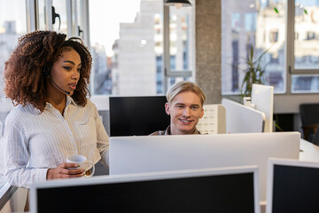 Customer service representative assisting colleague with computer issue in modern office