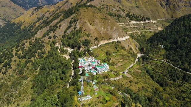 Aerial drone shot of a serene high-altitude village surrounded by dense forests and rolling green hills.