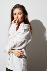 Model with long hair in a white shirt poses thoughtfully, creating a captivating image against a light background, perfect for fashion and portrait photography