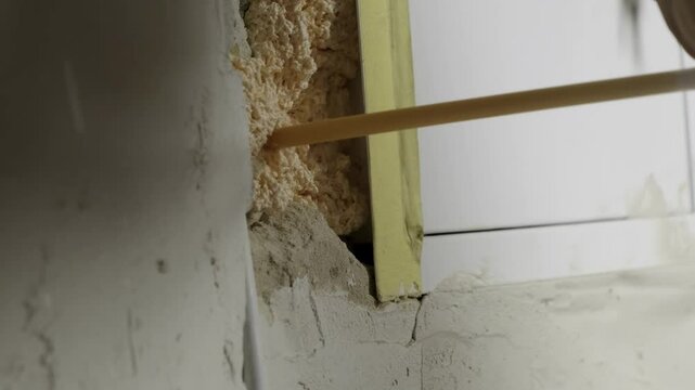Man construction worker applies expanding foam filling gaps in wall. Craftsman seals cavities with insulating foam during renovation process