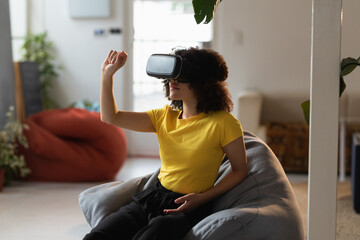 Woman in yellow shirt using VR headset, exploring virtual world at home