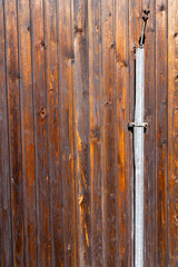 Metal element of a lightning rod mounted on the brown boards of the building's facade.