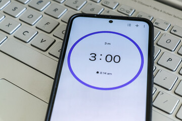 A phone with a black and white 3-minute timer to study with pomodoro method on laptop keyboard, study business background