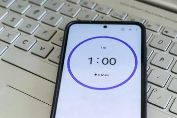 A phone with a black and white 1-minute timer to study with pomodoro method on laptop keyboard,...
