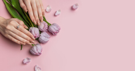 Woman showing stylish nude manicure with spring tulips on pink background